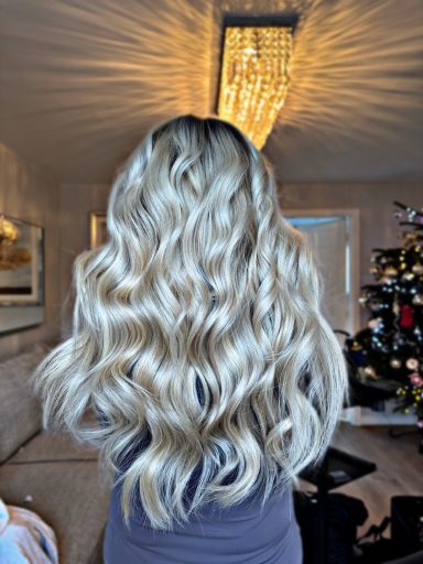 Long, wavy blonde hair cascading down the back, with a backdrop of a living room and Christmas tree.